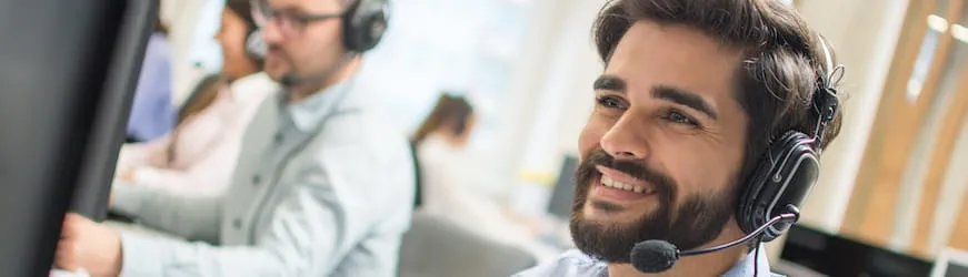 un jeune téléconseiller avec un casque audio devant un ordinateur