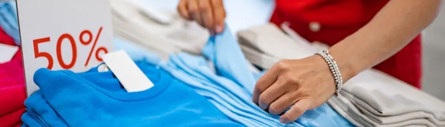 Des mains de femme qui plie une pile de vêtements en solde.
