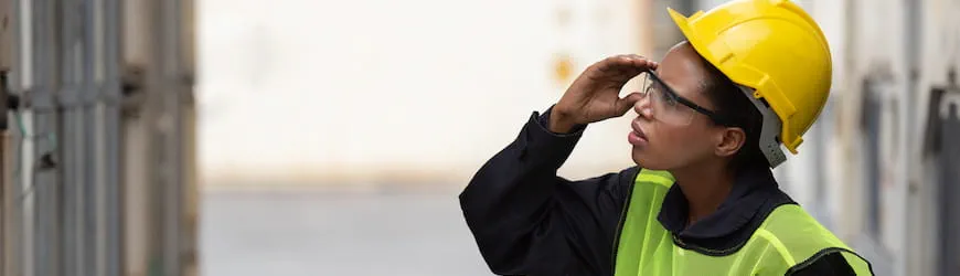 une salariée en casque et gilet de sécurité qui remarque un problème sur son lieu de travail