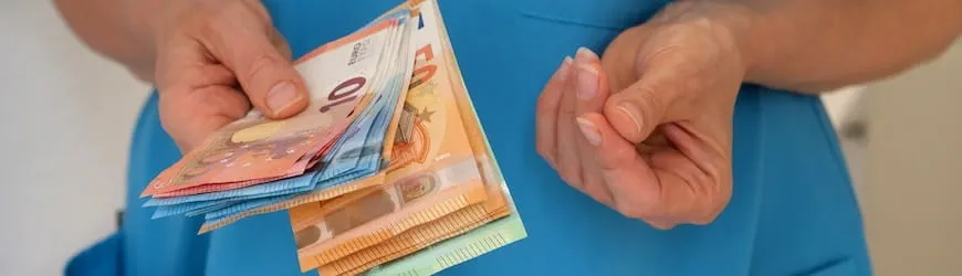 Les mains d’une salariée tenant des billets, qui calcule son salaire à temps partiel.