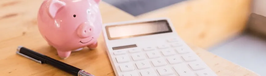 Une calculatrice posée à côté d’une tirelire, utilisée par un intérimaire pour calculer ses indemnités d’arrêt pour accident du travail.