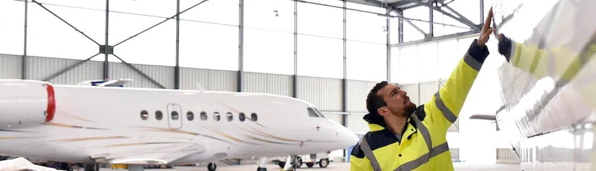 Un ajusteur-monteur aéronautique travaillant dans un hangar à côté de deux avions. 
