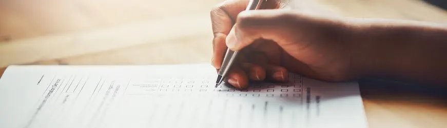 Une main qui écrit, en train de remplir un dossier de validation des acquis de l’expérience, ou VAE