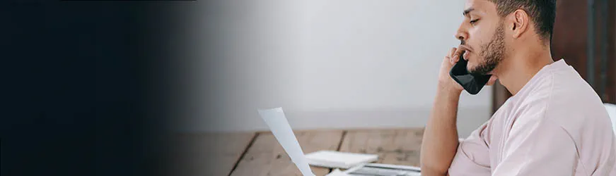 Jeune homme parlant au téléphone. Il lit un document qu’il tient à la main.