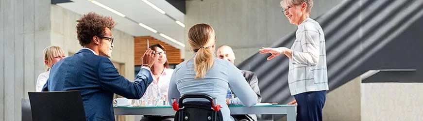 Six personnes dans un bureau, autour d’une table pendant une réunion. Une des personnes prenant part à la discussion est sur un fauteuil roulant, de dos Six personnes dans un bureau, autour d’une table pendant une réunion. Une des personnes prenant part à la discussion est sur un fauteuil roulant, de dos
