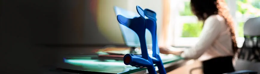 Une femme travaille à son bureau avec ses béquilles posées à côté d’elle