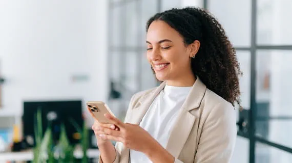 Une femme sourit en tenant son téléphone portable car elle a trouvé un travail grâce aux réseaux sociaux.