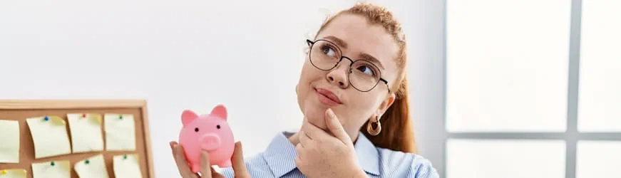 Une jeune femme qui réfléchit avec une tirelire dans la main