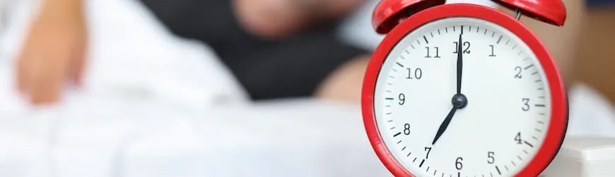 une homme qui dort à côté d’un réveil qui indique 7 heures