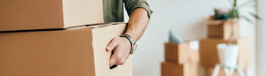 Un jeune homme, qui part travailler dans une autre ville, porte un carton de déménagement