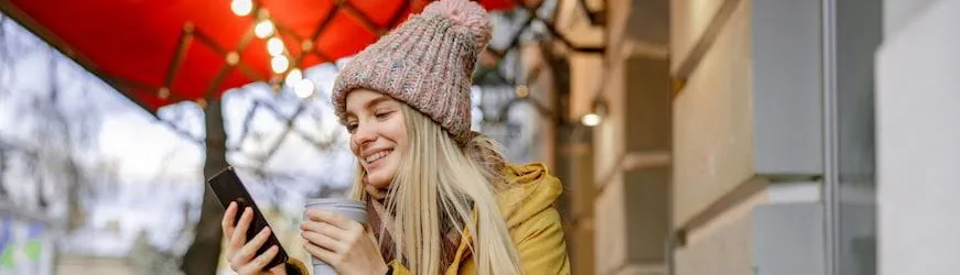 Une jeune femme en parka et bonnet, en train de chercher un job d’hiver insolite sur son téléphone