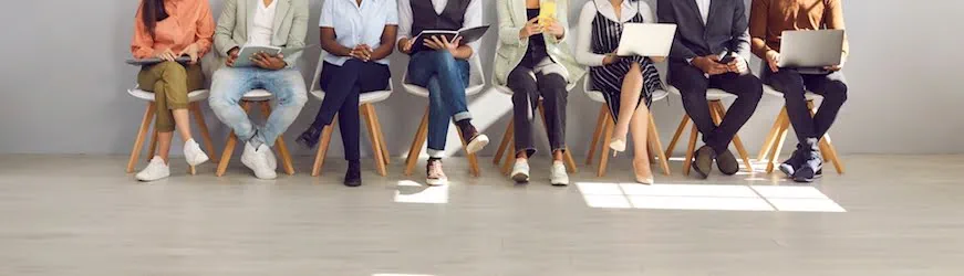 les jambes de plusieurs personnes qui cherchent un travail, assises dans une salle d’attente avant de passer leur entretien d’embauche