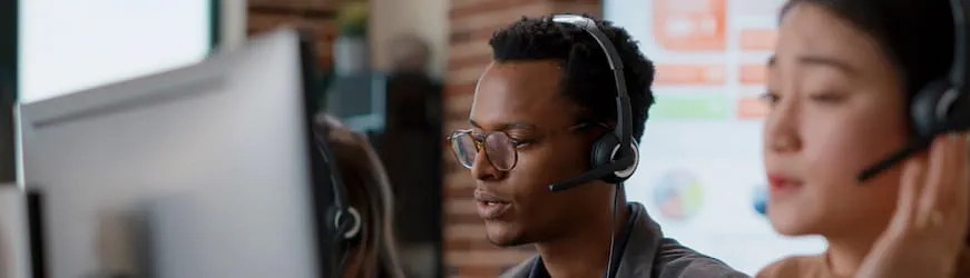 Un jeune homme avec un casque audio exerçant son métier en téléprospection, à côté d’une collègue