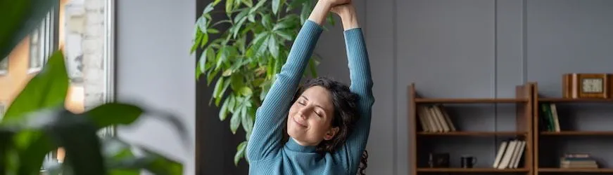 Une salariée assise à son bureau, en train de s’étirer pour profiter de sa pause au travail.