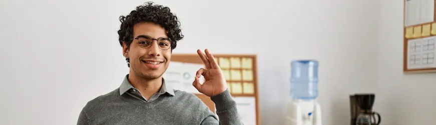 Un jeune homme souriant dans un bureau, qui s’est bien préparé à passer son entretien professionnel