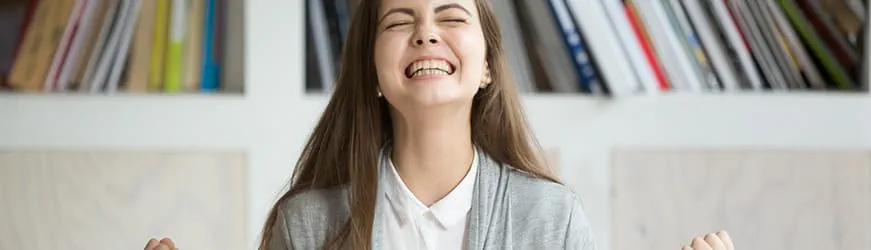 Jeune femme, devant son ordinateur, souriante et serrant les poings en signe de victoire.