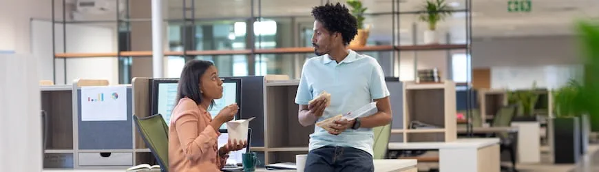 Deux collègues de travail en train de discuter à un bureau pendant leur pause déjeuner.