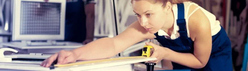 Une apprentie en menuiserie mesure une fenêtre dans un atelier. 