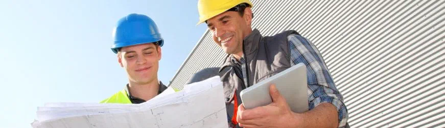 Un jeune apprenti en formation dans le BTP, en train de lire un plan de construction avec son employeur.