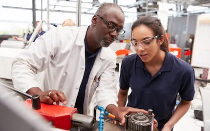 Un tuteur montrant à une apprentie comment fonctionne une machine industrielle. Un tuteur montrant à une apprentie comment fonctionne une machine industrielle.
