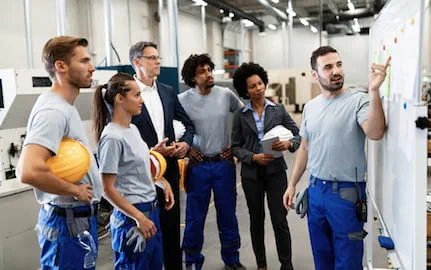Un jeune manager donne les consignes du jour à son équipe de techniciens et techniciennes, dans un atelier. Un jeune manager donne les consignes du jour à son équipe de techniciens et techniciennes, dans un atelier.