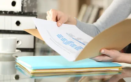 Les mains d'une personne en charge des ressources humaines, qui consulte un dossier pour connaîtres les règles à suivre en matière de recrutement.