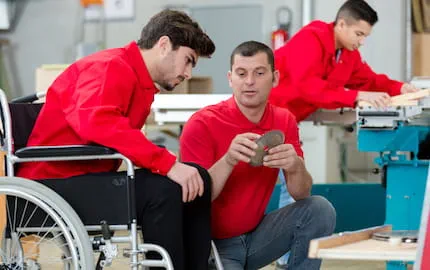 Un jeune apprenti en situation de handicap dans un atelier, en train d'écouter les explications de son tuteur. Un jeune apprenti en situation de handicap dans un atelier, en train d'écouter les explications de son tuteur.