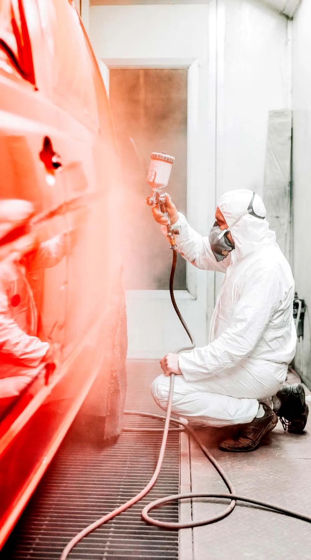 Trabajador pintando un vehículo con pistola en una cabina de pintura industrial Trabajador pintando un vehículo con pistola en una cabina de pintura industrial
