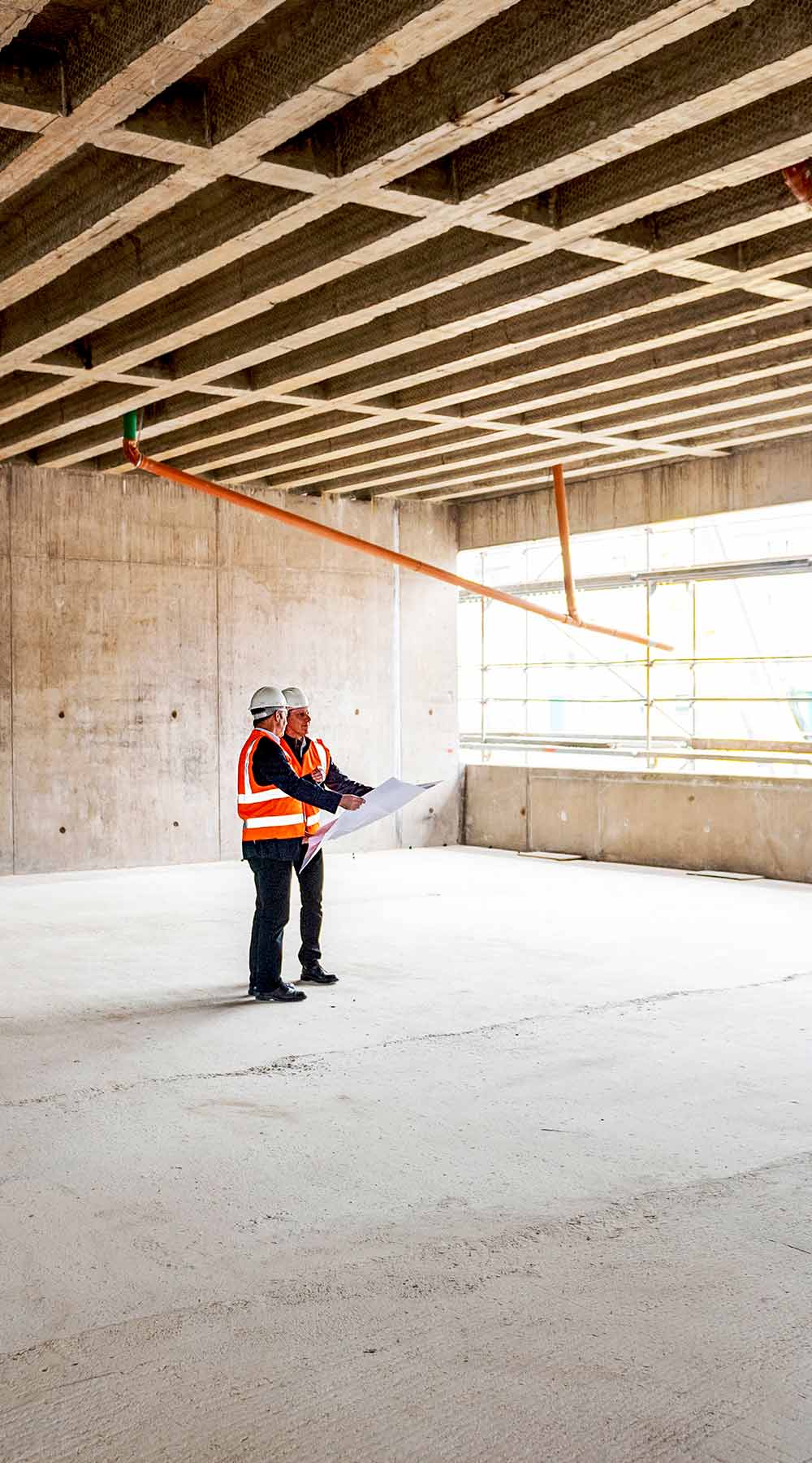 Dos trabajadores de pie en el gran interior de un edificio inacabado