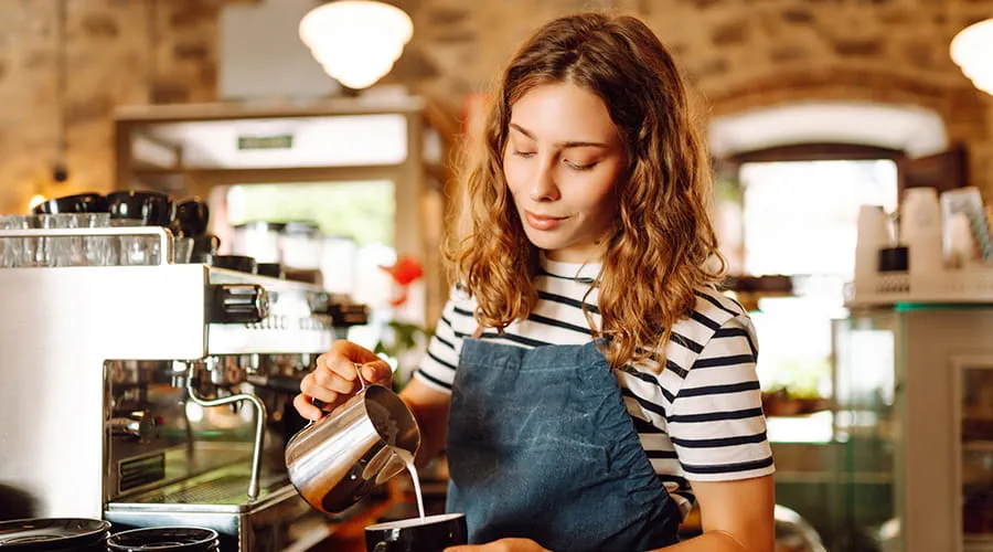 Una barista está detrás del mostrador, sirviendo café recién hecho