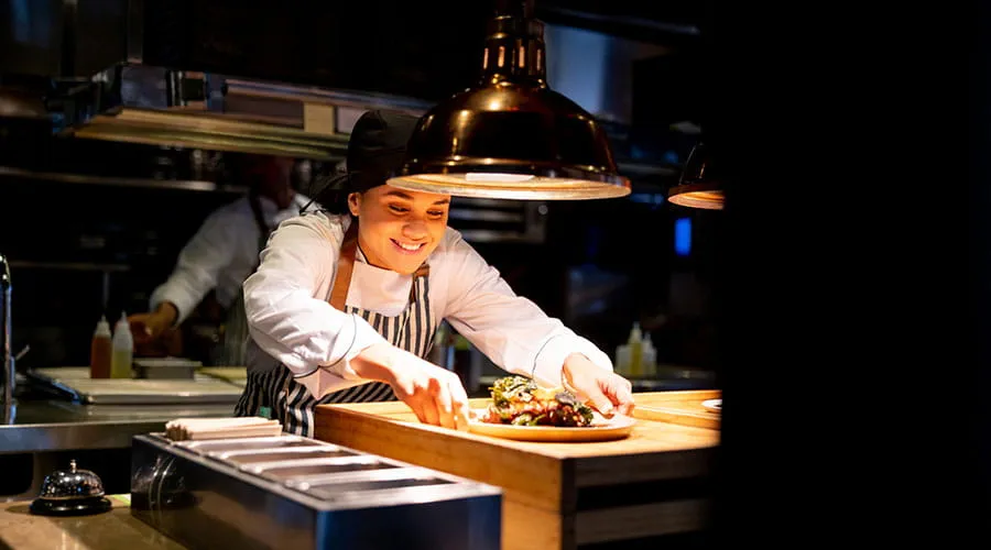 Chef colocando un plato bajo una lámpara caliente en una cocina comercial Chef colocando un plato bajo una lámpara caliente en una cocina comercial