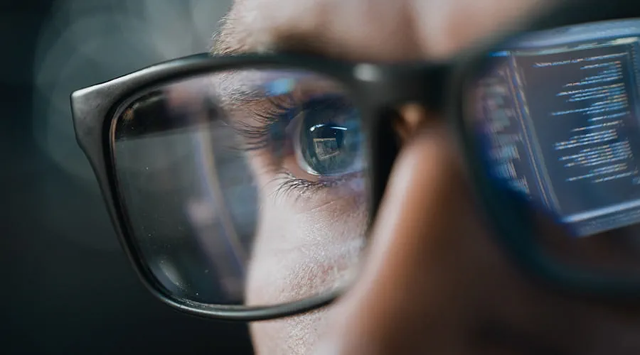 Primer plano hombre con gafas revisando datos reflejo ordenador