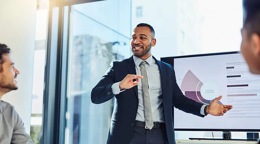 Hombre de negocios mostrando unos gráficos en una pantalla a dos personas Hombre de negocios mostrando unos gráficos en una pantalla a dos personas