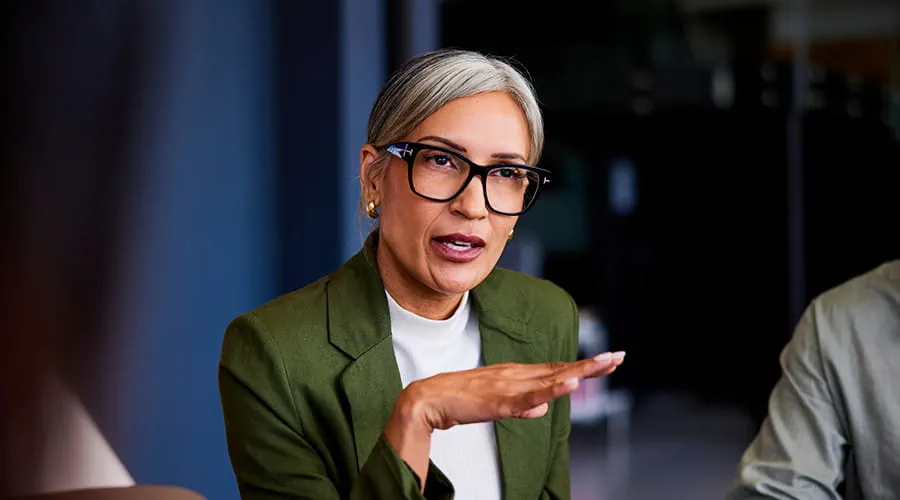 Mujer de negocios con cabello gris y gafas, gesticulando y explicando Mujer de negocios con cabello gris y gafas, gesticulando y explicando
