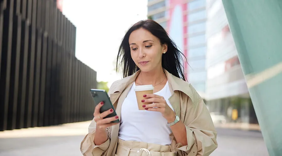 Mujer joven antando por la calle revisando su teléfono inteligente Mujer joven antando por la calle revisando su teléfono inteligente