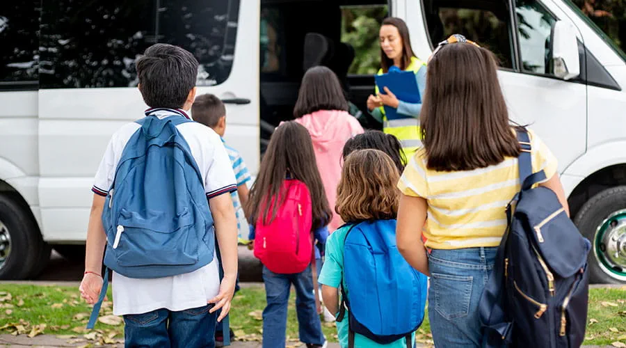 Niños y niñas de espalda con mochilas acercándose al autobús escolar Niños y niñas de espalda con mochilas acercándose al autobús escolar