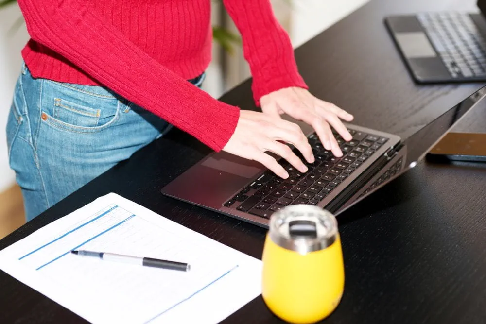 Les mains d'une salarié travaillant sur son ordinateur portable portant un pull rouge Les mains d'une salarié travaillant sur son ordinateur portable portant un pull rouge