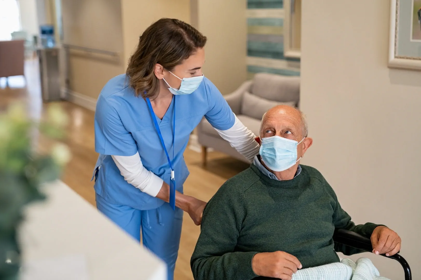 Une infirmière portant un masque aide un patient âgé en fauteuil roulant Une infirmière portant un masque aide un patient âgé en fauteuil roulant