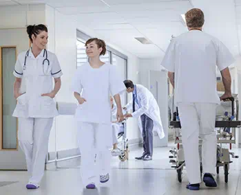 Deux infirmières souriantes marchent dans le couloir d'un hôpital et un infirmier pousse un brancard à côté Deux infirmières souriantes marchent dans le couloir d'un hôpital et un infirmier pousse un brancard à côté