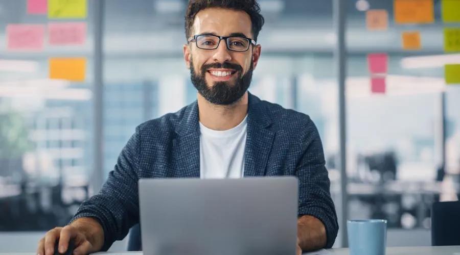 Male professional smiling while working on a laptop in an office