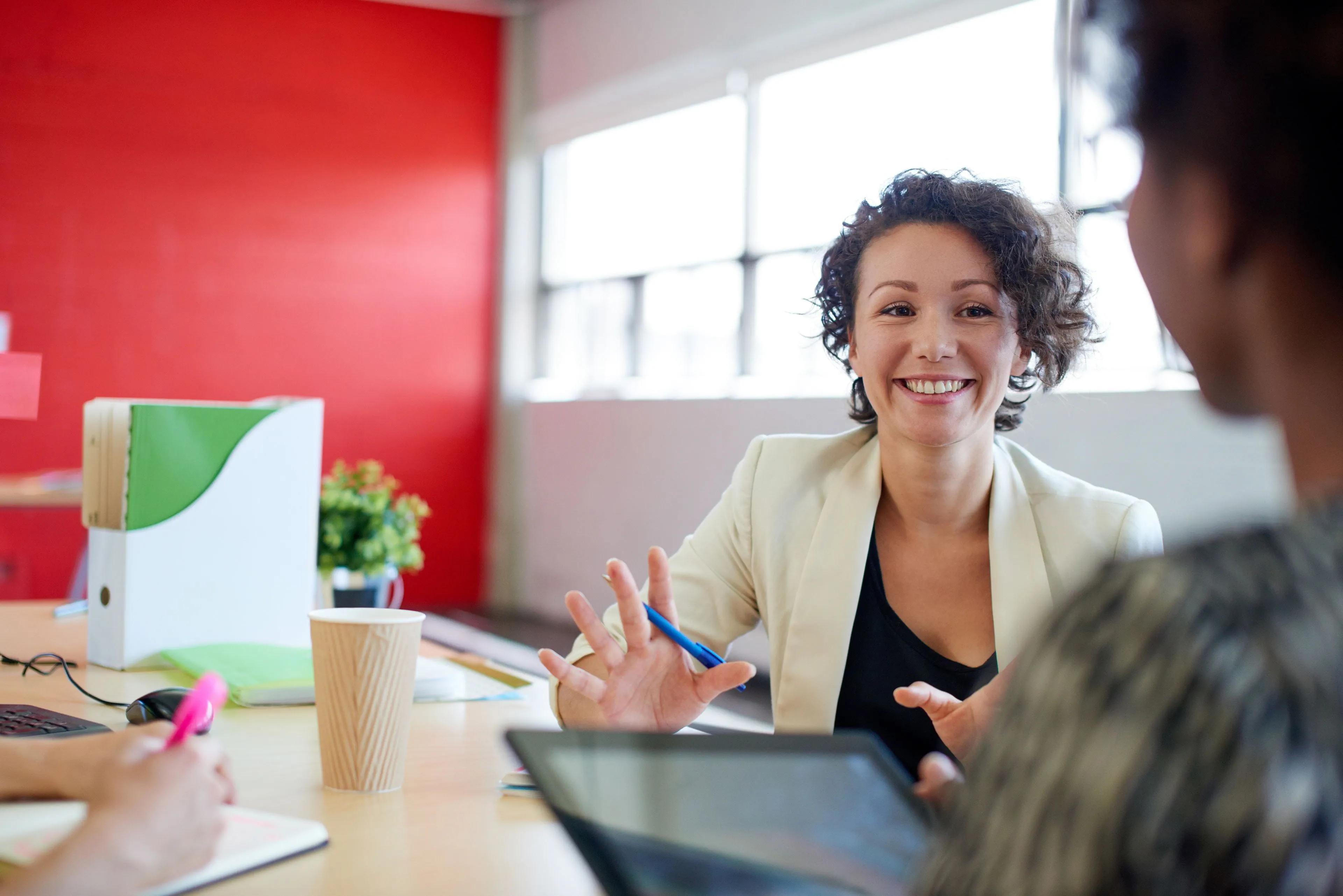 Woman sitting at a meeting room table in a work setting speaking to a colleague
