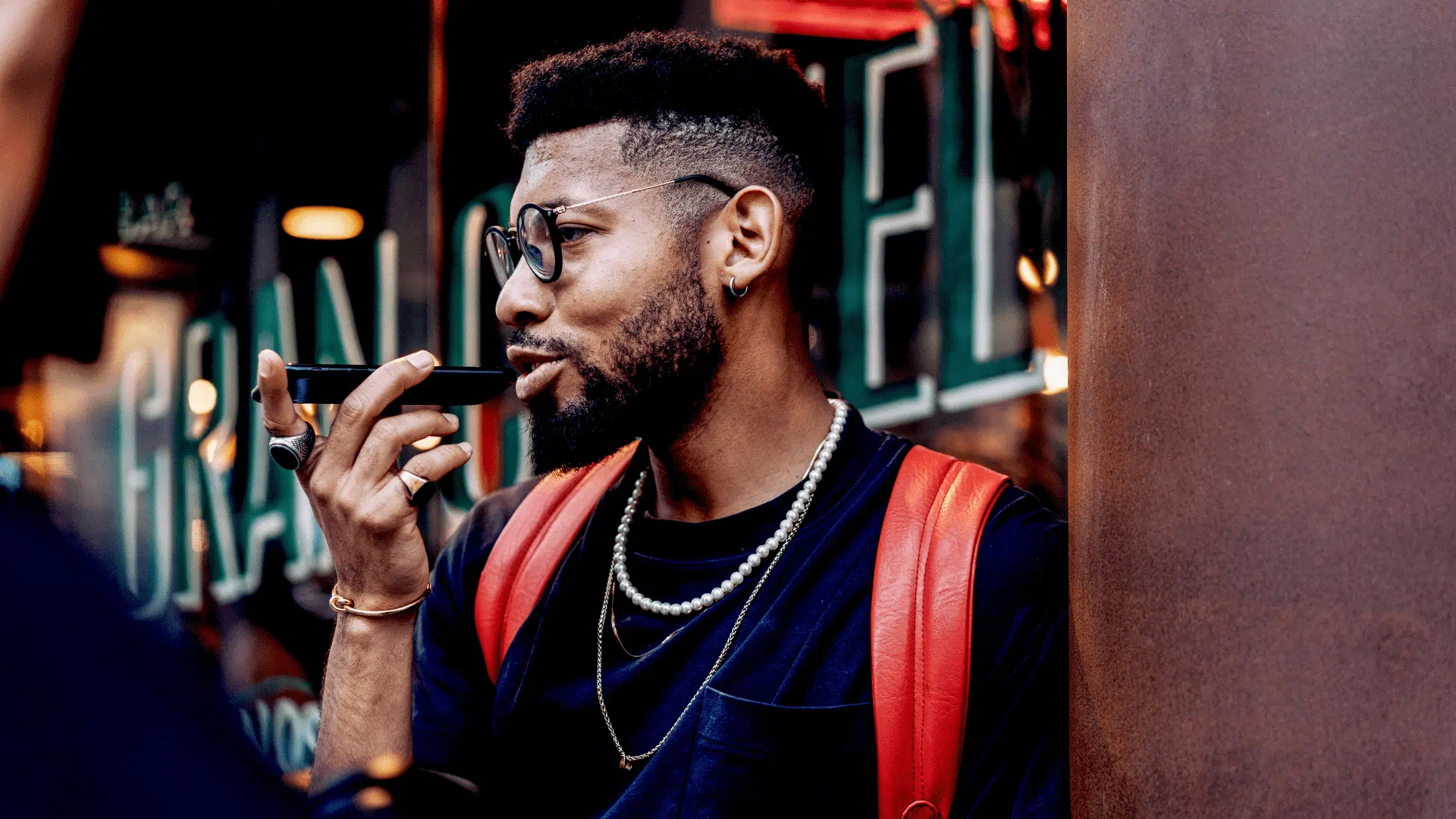 man wearing glasses and a red backpack speaking on the phone outside man wearing glasses and a red backpack speaking on the phone outside