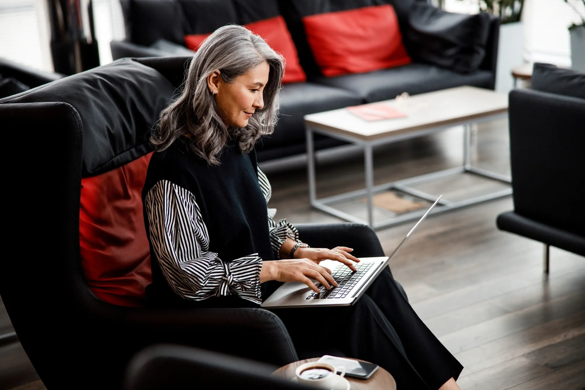 A businesswoman sitting in an armchair in her office, working on a modern laptop