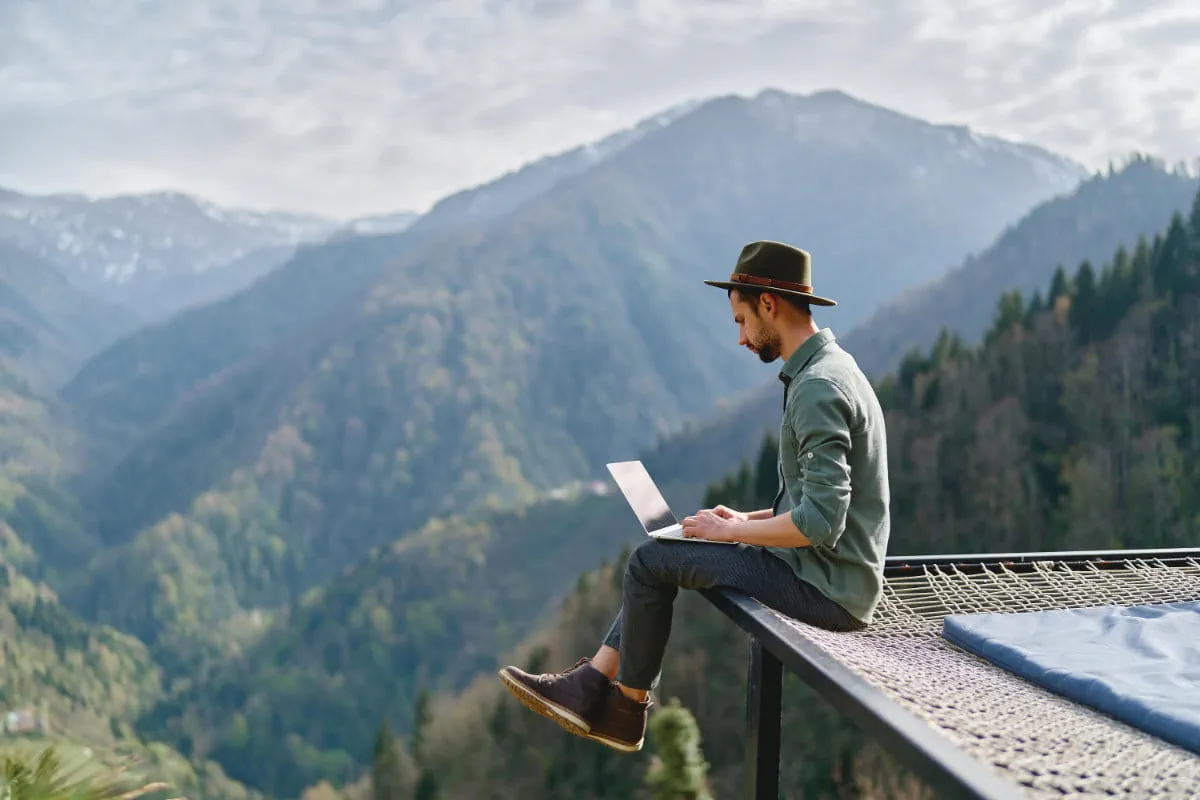 person-sitzt-auf-einer-plattform-in-den-bergen-und-arbeitet-am-laptop person-sitzt-auf-einer-plattform-in-den-bergen-und-arbeitet-am-laptop