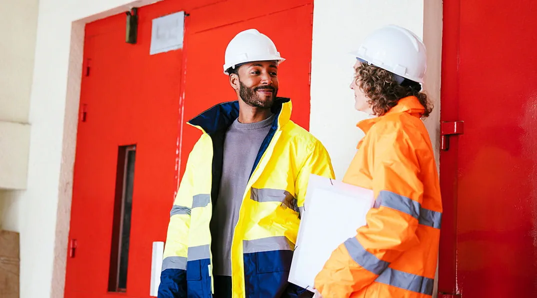 Twee collega's met bouwhelmen overleggen met elkaar Twee collega's met bouwhelmen overleggen met elkaar
