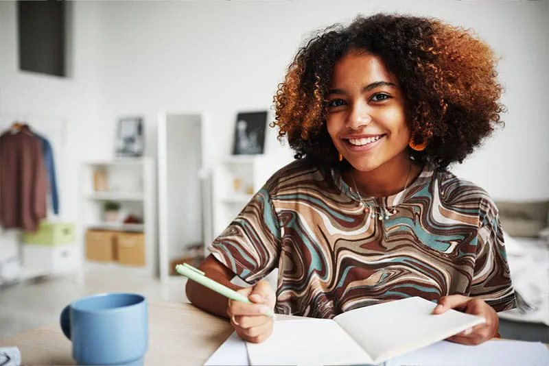 Woman writing notes in a notebook while smiling at a desk Woman writing notes in a notebook while smiling at a desk