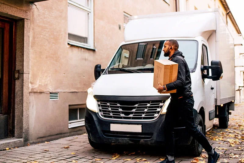 Delivery driver carrying a package from a delivery van outside a residential building.
