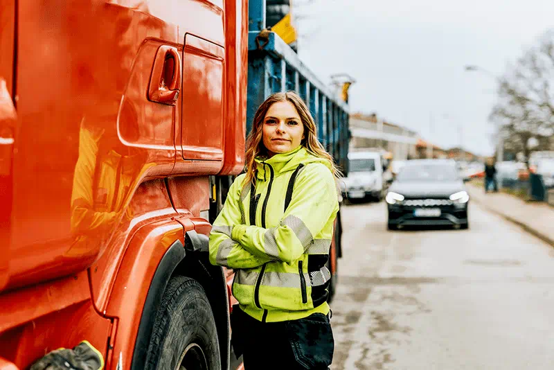 Female truck driver and logistics professional standing next to a commercial vehicle in high-visibility workwear, highlighting careers in transport and logistics.