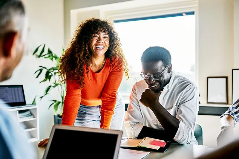 Team members smiling and collaborating around a meeting table during a discussion in a bright, modern office. Team members smiling and collaborating around a meeting table during a discussion in a bright, modern office.