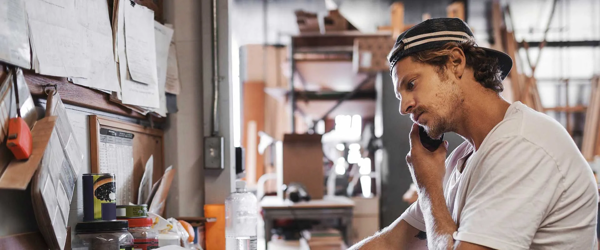 Travailleur masculin dans un atelier parlant au téléphone tout en gérant les tâches Travailleur masculin dans un atelier parlant au téléphone tout en gérant les tâches